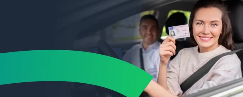 Uśmiechnięta młoda kobieta odbierająca prawo jazdy w samochodzie egzaminacyjnym po zdanym egzaminie państwowym 2026